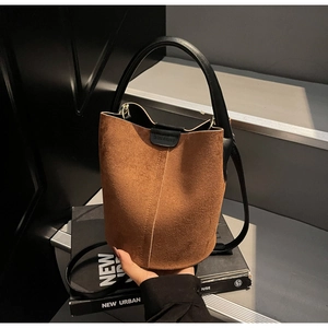 Detail of dark brown suede bucket bag featuring leather handle and gold hardware