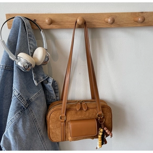 Detail of a brown matte suede Boston bag featuring dual zippers and a beaded wooden charm