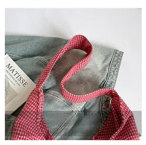Close-up of durable woven strap on red and white checkered canvas handbag with stitching