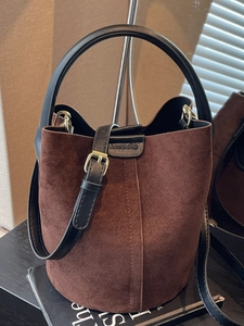 Brown matte suede bucket bag with black leather handle and adjustable shoulder strap