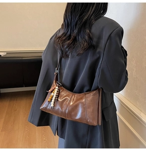 Sac hobo marron sous le bras avec breloque en perles sur une veste grise chic