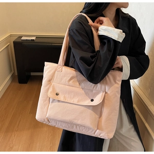 Close-up of a light pink tote bag with wide handles and a large snap-button front pocket