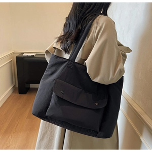 Detail of black nylon tote bag with large flap pocket and metallic button closure
