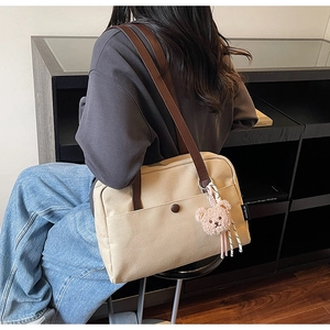 Detailed back view of a beige canvas tote bag with brown leather straps and pink bear charm