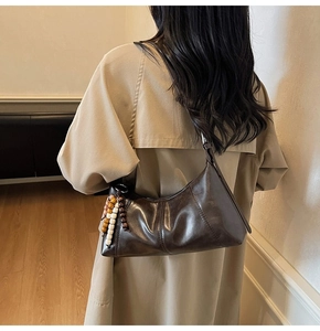 Détail d'un sac hobo marron foncé avec un gland perlé dans un décor intérieur cosy