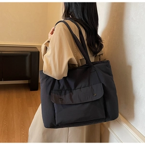 Detail view of a large black tote bag featuring a functional front flap pocket with snaps