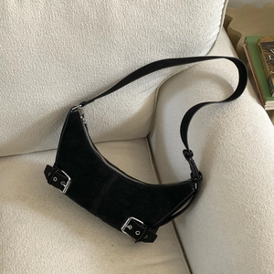 Gros plan d'un sac hobo en daim noir avec boucles argentées sur un canapé blanc cassé