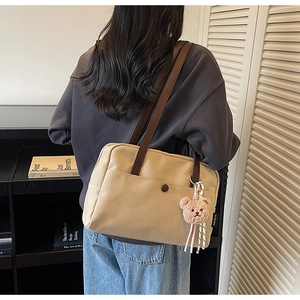 Detail of beige canvas tote bag with brown leather straps and cute plush bear charm