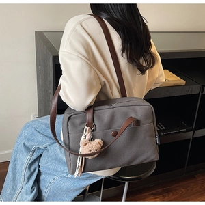 Detail of dark grey canvas bag with brown leather strap and cute bear charm accessory