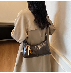 Détail d'un sac à bandoulière vintage en cuir marron foncé avec charme perlé sur un manteau