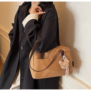 Detail of khaki canvas tote with brown leather strap and plush bear charm on model