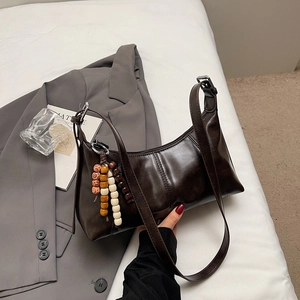 Détail d'un sac sous le bras marron foncé avec breloque ethnique sur draps blancs