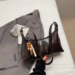 Détail d'un sac sous le bras marron foncé vintage avec charme en perles de bois et bandoulière