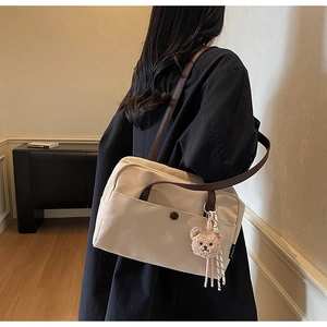 Detail of canvas tote bag with brown straps and cute teddy bear charm hanging on the side
