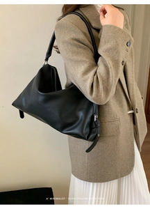 Minimalist black pebbled leather underarm bag shown on a model with a wool coat