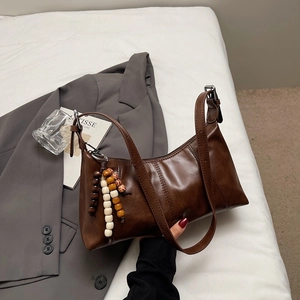 Détail du sac rétro marron foncé avec breloque en perles de bois sur literie blanche