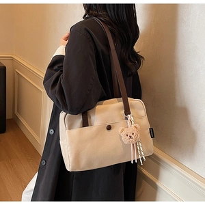 Detail of beige canvas tote with brown straps, front pocket, and plush bear charm