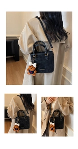 Close-up of black crossbody bucket bag with elegant plush bear charm and handle detail