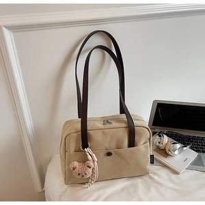 Detailed close-up of khaki canvas tote bag featuring brown leather handles and bear charm