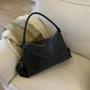 Close-up of black lychee texture leather shoulder bag on a cream sofa in a cozy room