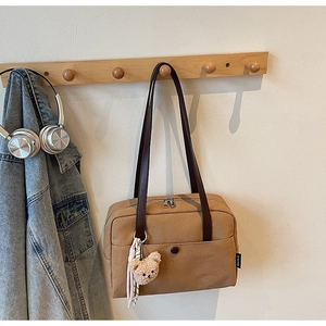 Detail of khaki tote bag featuring zip closure, front pocket, and cute plush bear charm