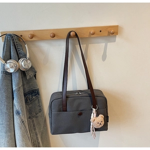 Close-up of a grey canvas tote bag featuring brown leather handles and a bear charm