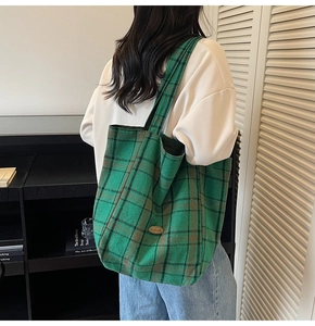 Detail of green plaid canvas tote bag with handmade label worn by model in casual style