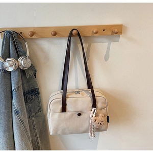 Beige canvas Boston bag on a wall hook featuring brown straps and a cute teddy pendant