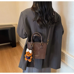 Brown vintage leather bucket bag with teddy bear charm shown on person's shoulder