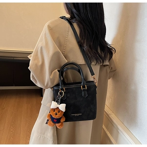 Black leather bucket bag with gold hardware and plush bear charm shown on model