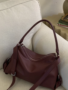 Deep burgundy pebbled leather tote bag in a half-moon shape on a cozy cream sofa