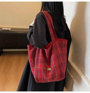 Detail of red plaid canvas tote bag with a handmade metal tag and spacious design