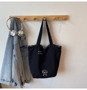 Detail of black canvas tote bag with dog print and checkered lining on wood hook