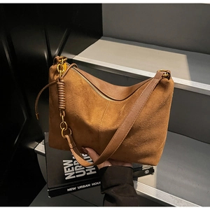 Dettaglio borsa a spalla in camoscio marrone con tracolla intrecciata e cerniera dorata