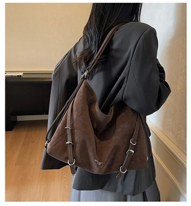 Detail view of large dark brown suede tote bag with silver metal buckles on gray blazer