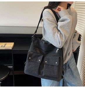 Detail view of black canvas tote bag with front flap pockets and silver metal zippers