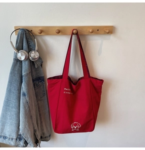Detail of red canvas tote bag with cartoon dog print hanging on wooden hook with denim jacket