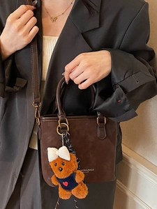 Coffee brown suede bucket bag with plush bear charm worn by a model in a minimalist setting