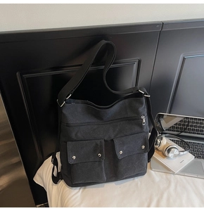 Detail view of black canvas multi-pocket tote bag with metal buttons and laptop on white table