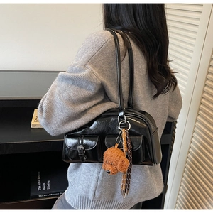 Side view of shiny black Boston bag with functional pockets and a plush dog charm