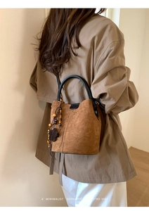 Close-up of brown suede bucket bag with wooden bead tassels and leather handle detail