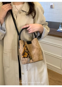 Detail of retro brown suede bucket bag with wooden bead charm and black leather handle