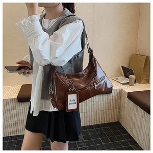 Detail of a dark brown oil wax faux leather tote bag worn by a model in a cozy cafe setting