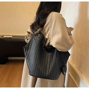 Détail de la texture d'un grand sac cabas en cuir tressé noir porté par un mannequin