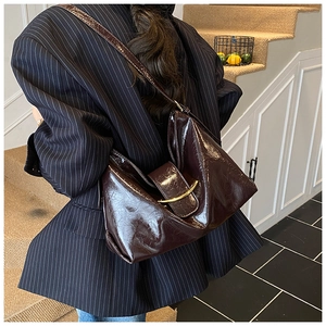 Détail d'un cabas en cuir ciré marron foncé avec boucle dorée porté par un mannequin en costume