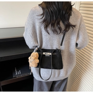 Detail of matte black crossbody bag with silver twist lock and plush bear pendant accessory