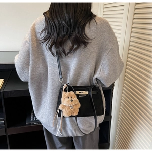 Detail of matte black crossbody bag with brown plush bear charm and silver twist lock
