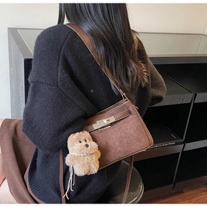 Detail of a brown matte suede square handbag with a cute dog charm and silver clasp