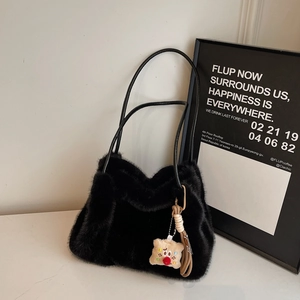 Dettaglio di borsa in peluche nera con tracolla in pelle e ciondolo a forma di orsetto