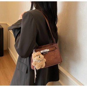 Detail view of brown suede shoulder bag featuring silver hardware and plush dog pendant
